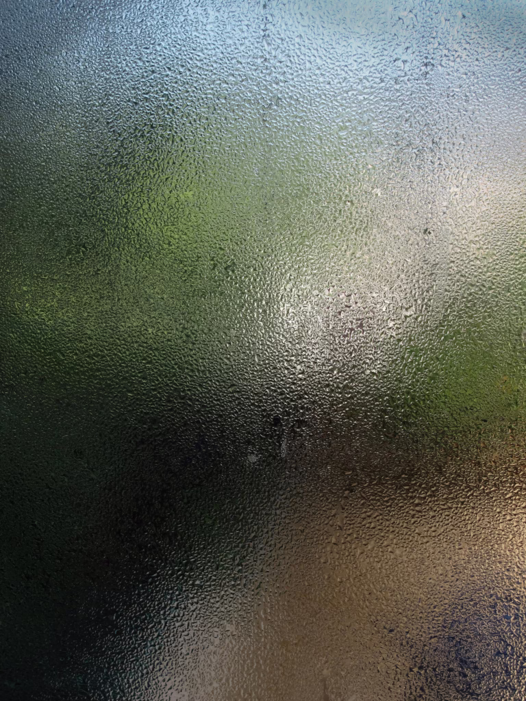 Close-up view of a wet glass pane with water droplets creating a blurred background effect.